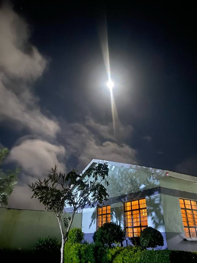 A school building with lit windows under a bright moon and clouds